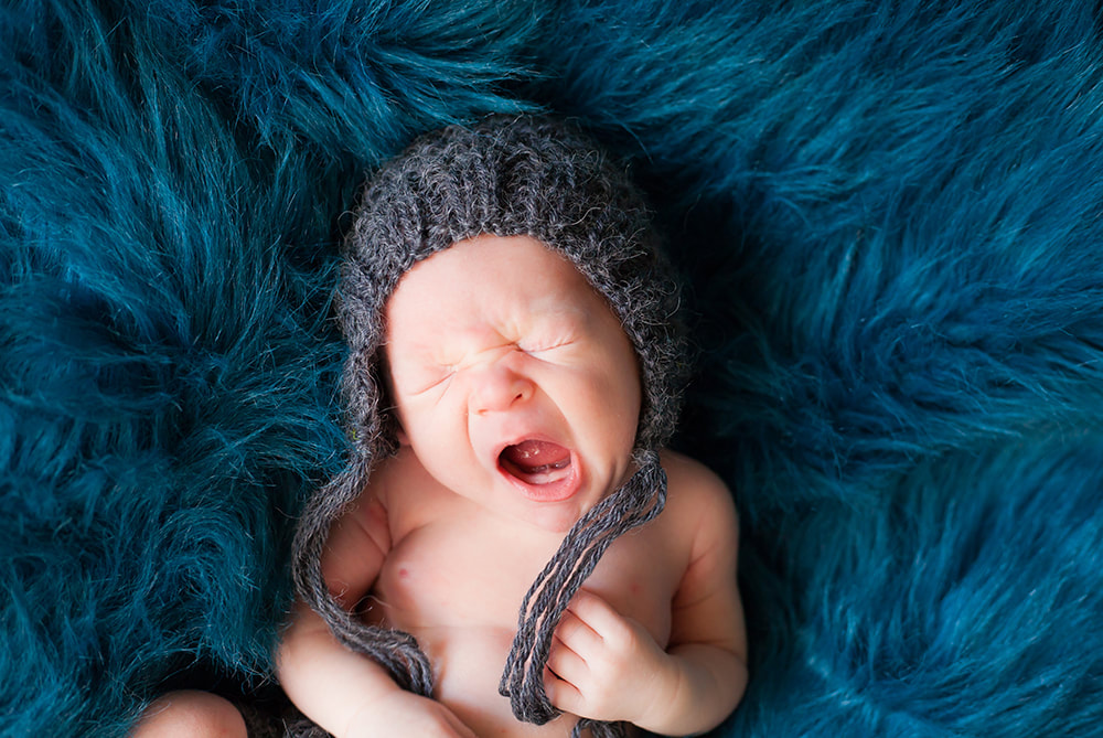 Close up of newborn baby yawning on a blue fur background