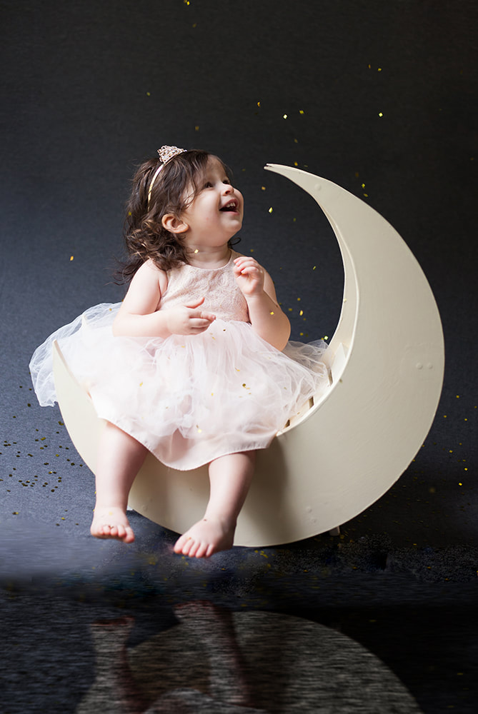 toddler sits on a moon with her reflection below her