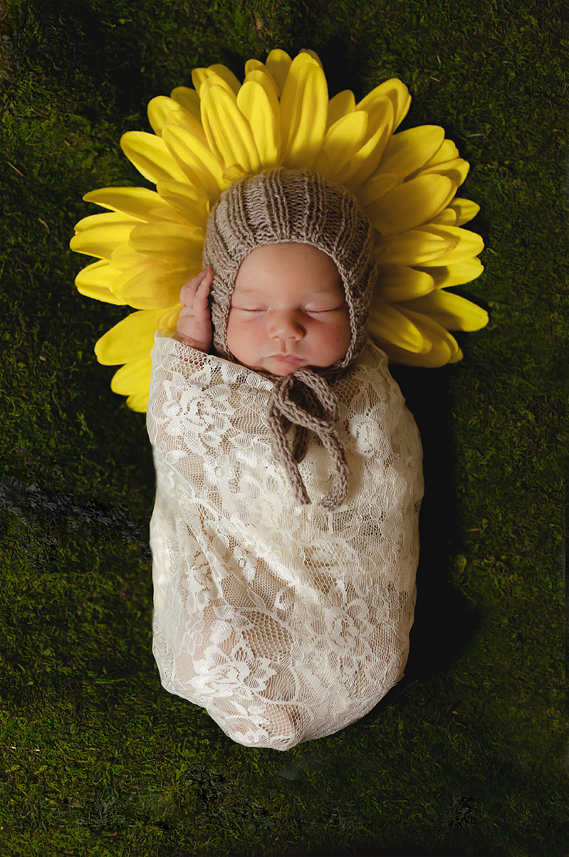 Newborn baby wrapped in lace lies on moss with flower petals coming out around her head