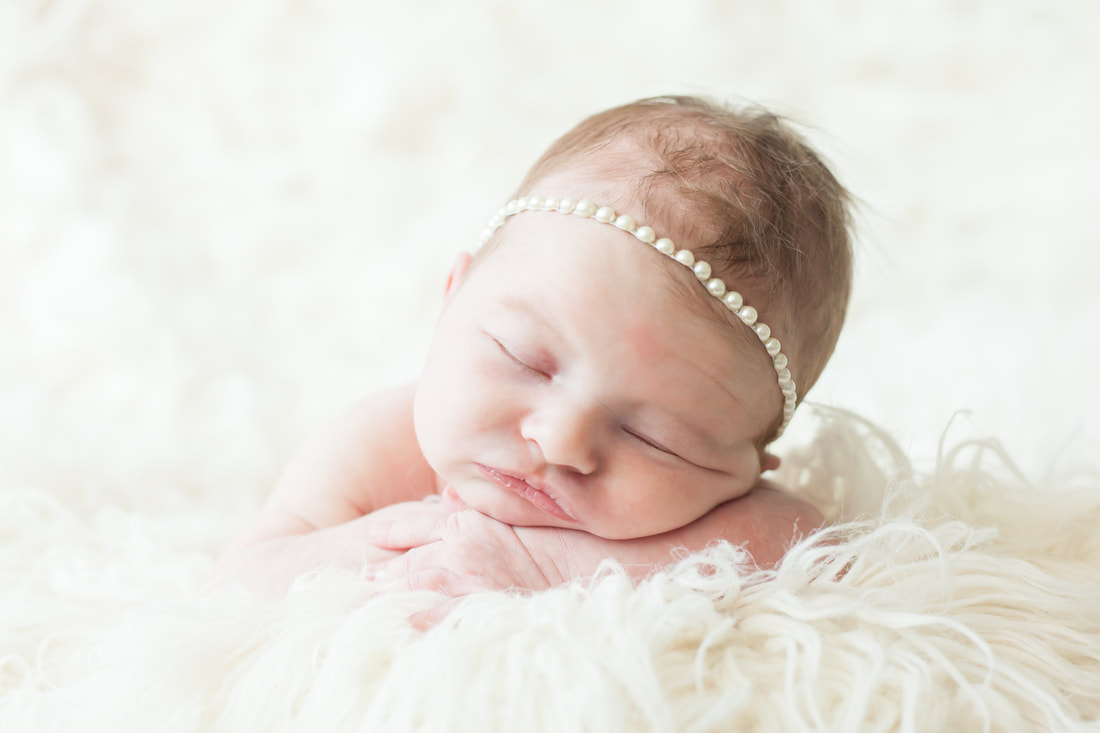 baby wearing a pearl headband sleeps on a cloud of white fur