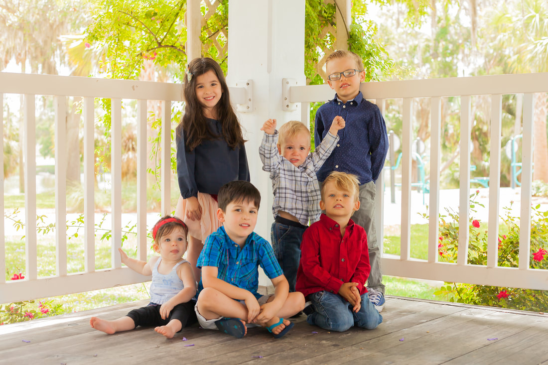 Six Children pose together in front of white picket fence 