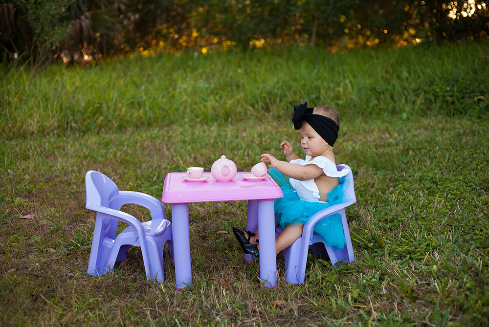 One year old baby girl having a tea party in a dreamy field