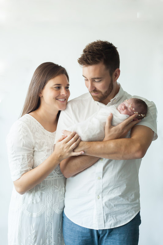 mother, father and newborn baby pose together in all white 