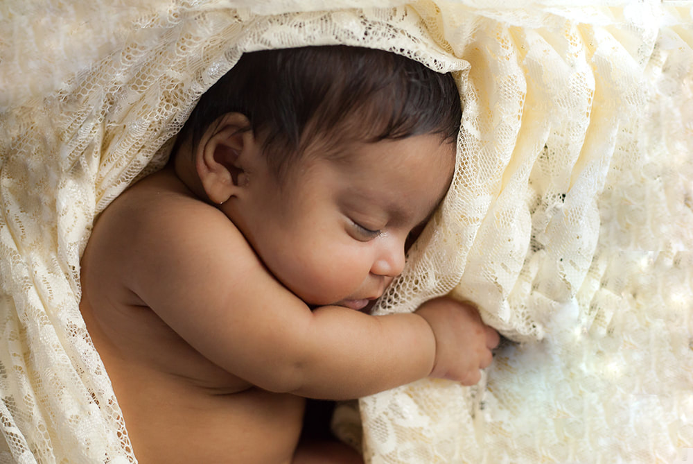 newborn baby sleeping surrounded by lace 