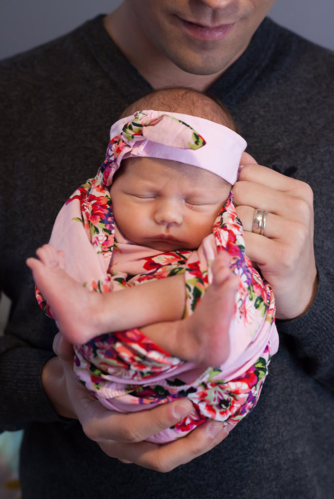 Father holds his newborn baby girl swaddled with a flower wrap
