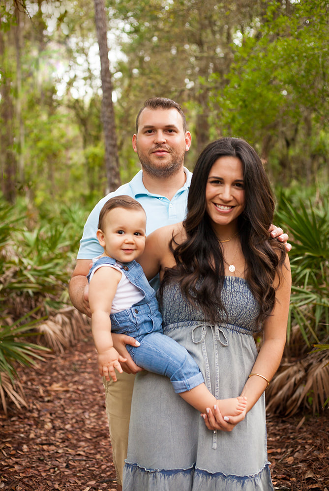 Parents and their one year old baby smile at camera in a tropical forest