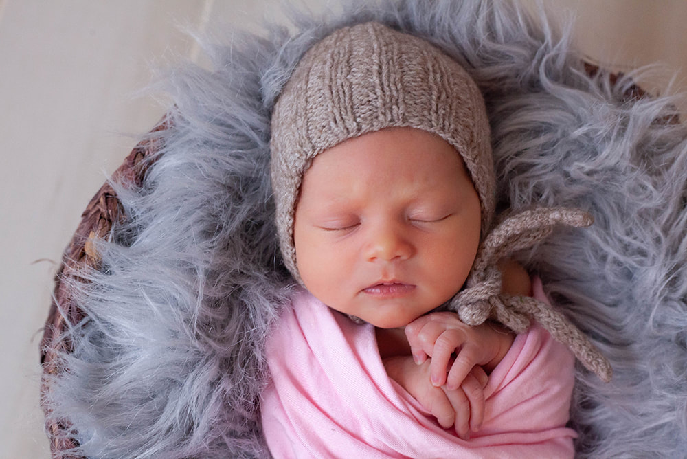 Newborn baby wearing bonnet and sleeping in a wicker basket