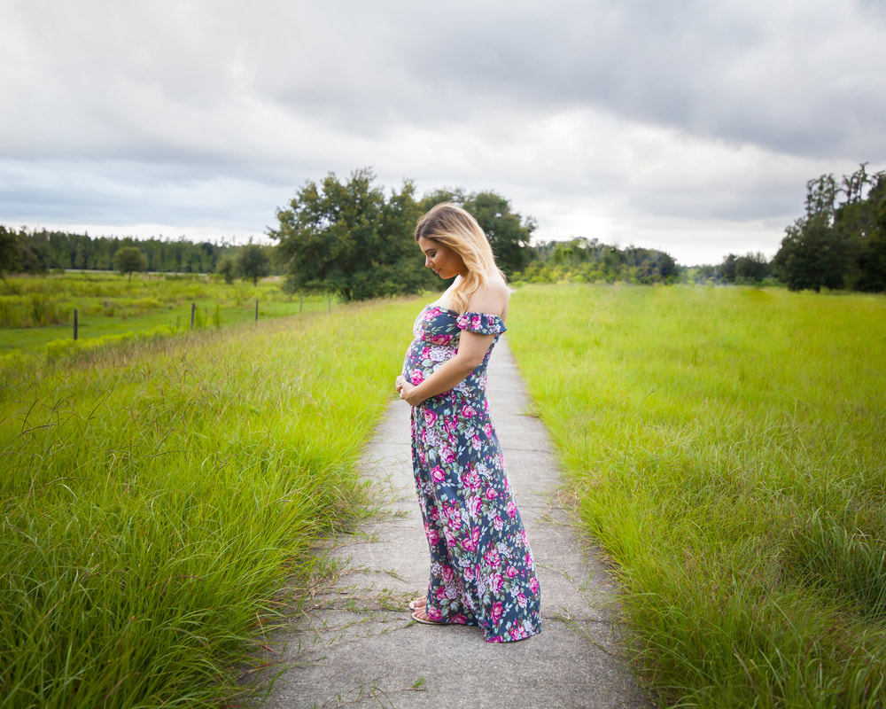 Pregnant woman standing in open wind swept field in Wesley Chapel Florida looking down at belly
