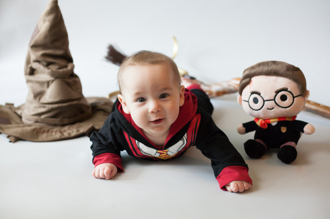 Baby in harry potter costume lying on stomach with harry potter props. 