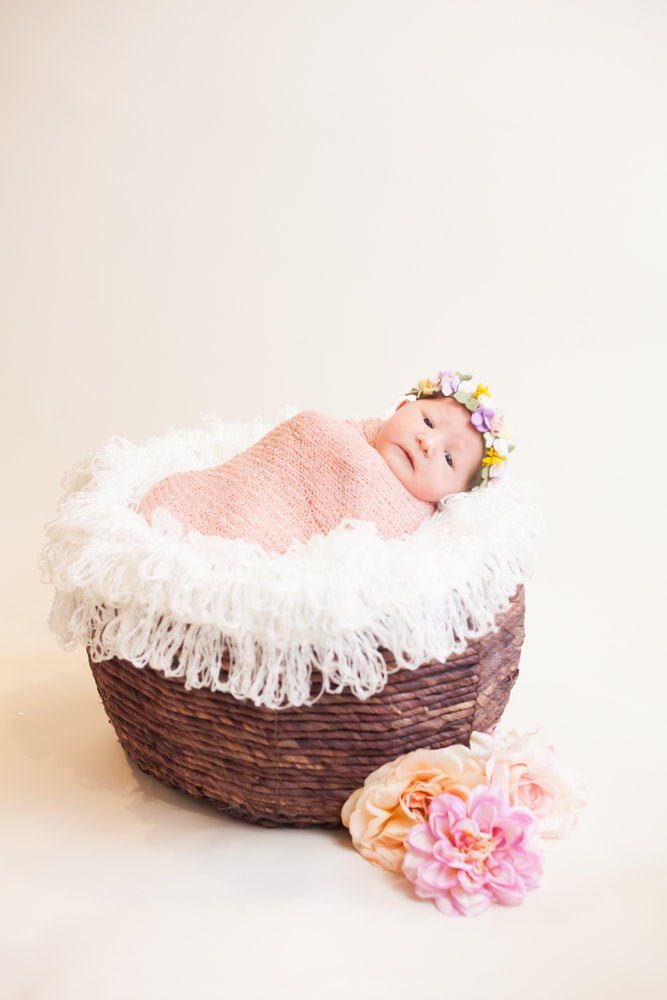 In home photograph of newborn baby swaddled and lying in a brown basket