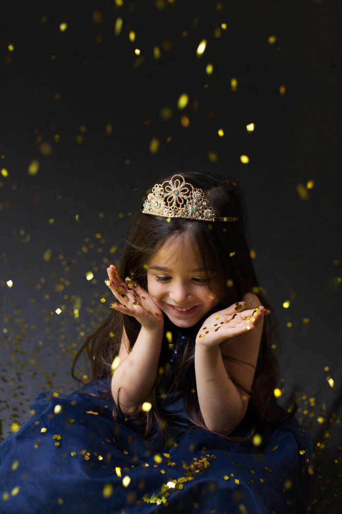 Five year old smiles as confetti falls around her in a photo studio in Tampa