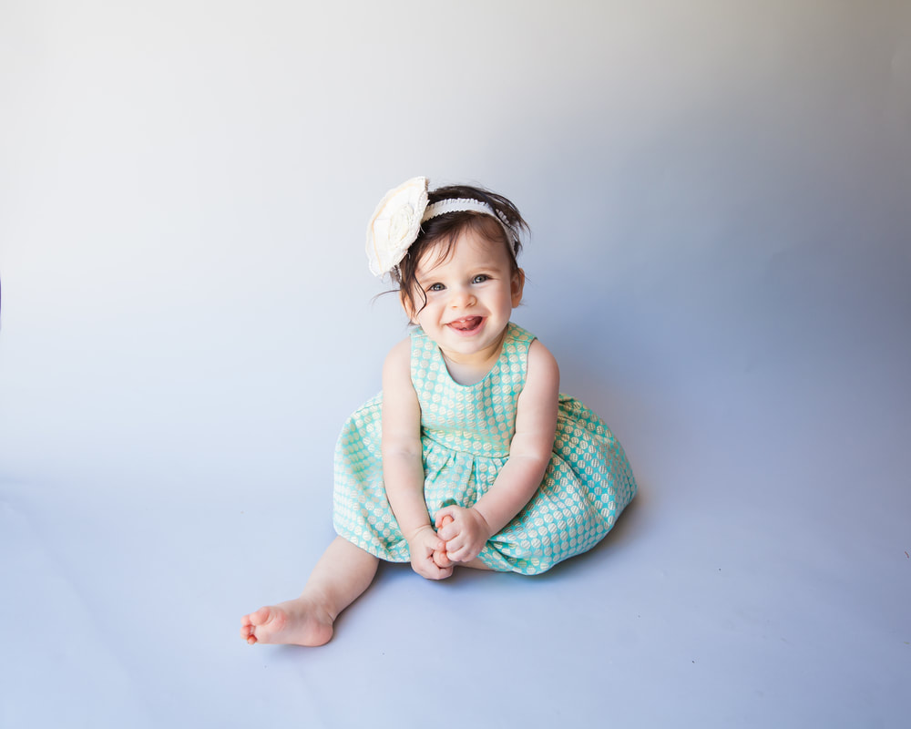 Baby girl smiling while sitting on light blue background with green and gold dress