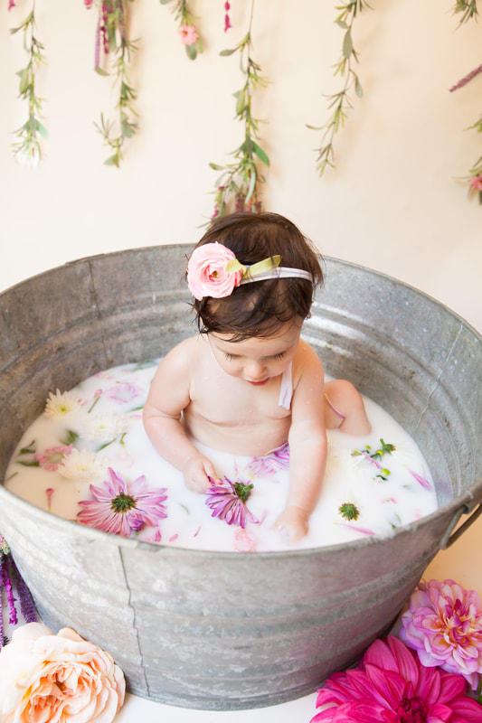 Sweet baby girl sits in milk bath in galvanized tub