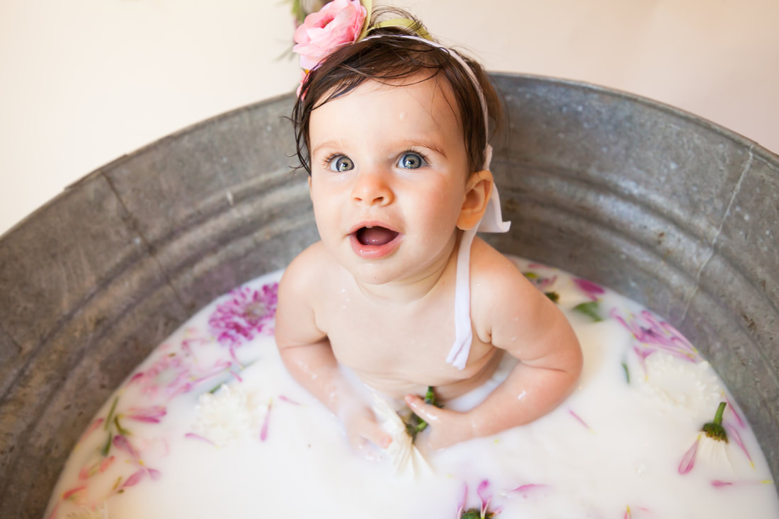 Cute baby with big blue eyes in a milk bath with flowers