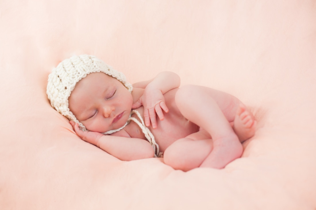 Newborn wearing white bonnet on pink background