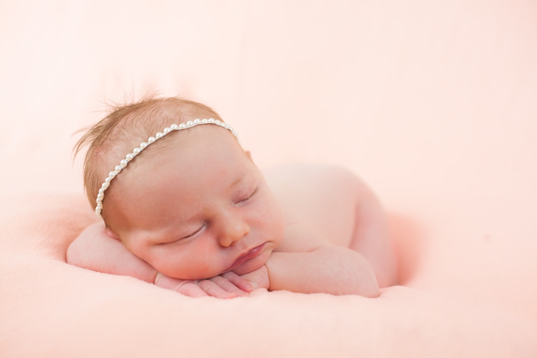 Newborn baby with headband on pink background