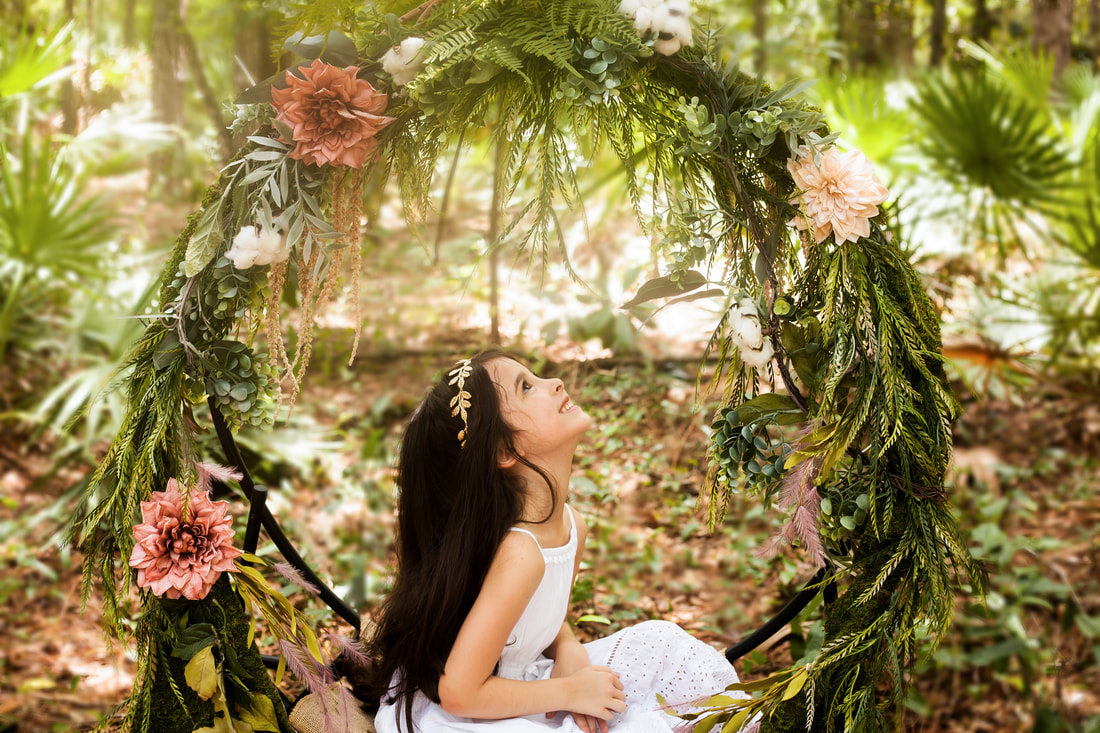 A little girl sits in a flower swing looking up and smiling