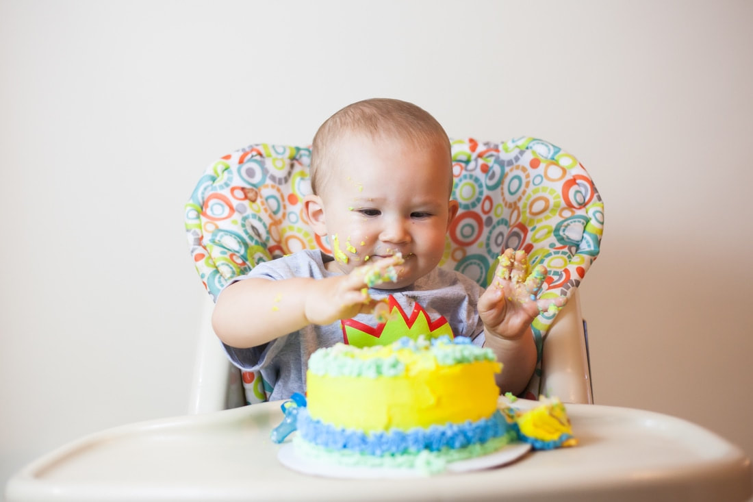 Smiling baby on white background digs in to his birthday cake
