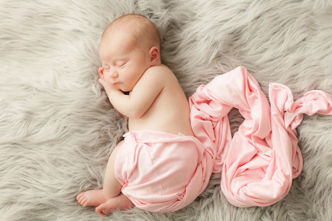 Sleeping newborn baby on gray fur with a pink wrap around her
