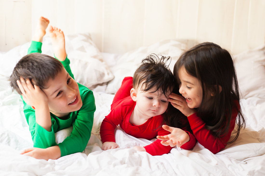 Three Children lie on their tummies laughing in red and green pajamas. a baby girl in red, a little boy in green, and a little girl in red. The image is bright and cheery