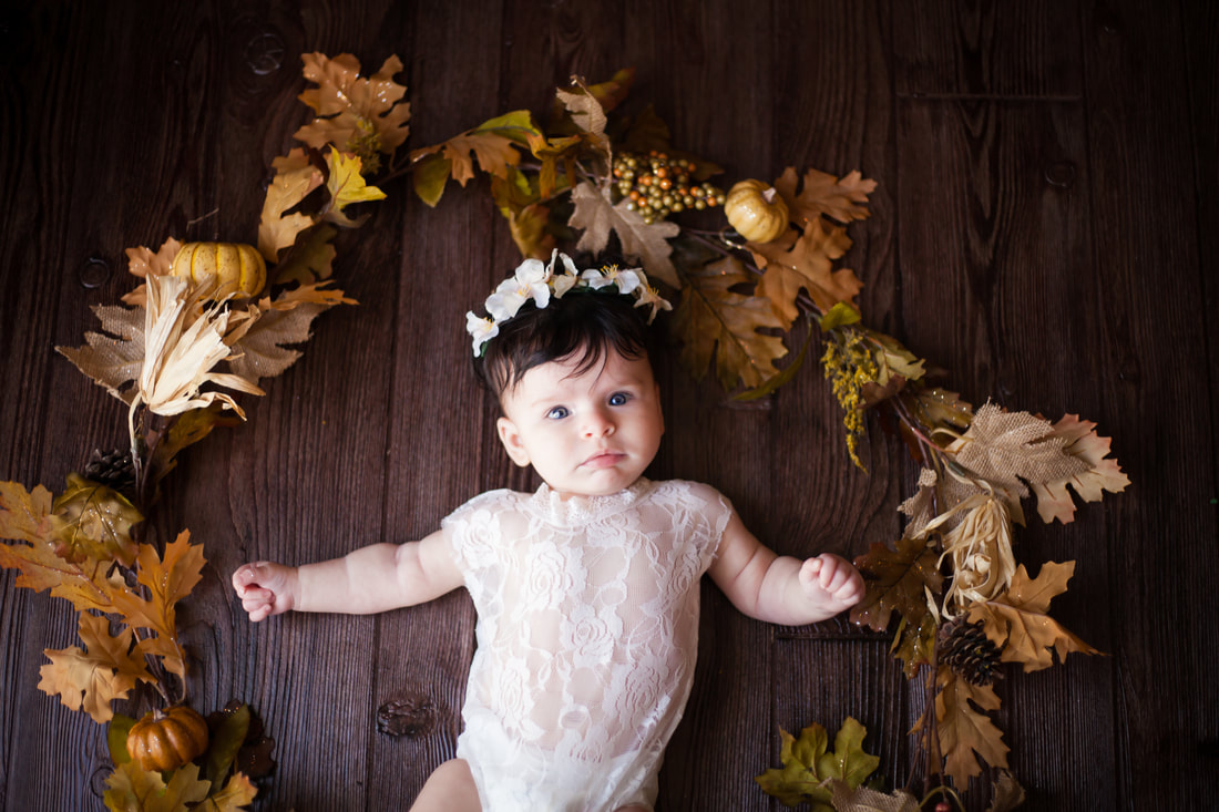 Baby girl in rich fall photograph with leaves all around her