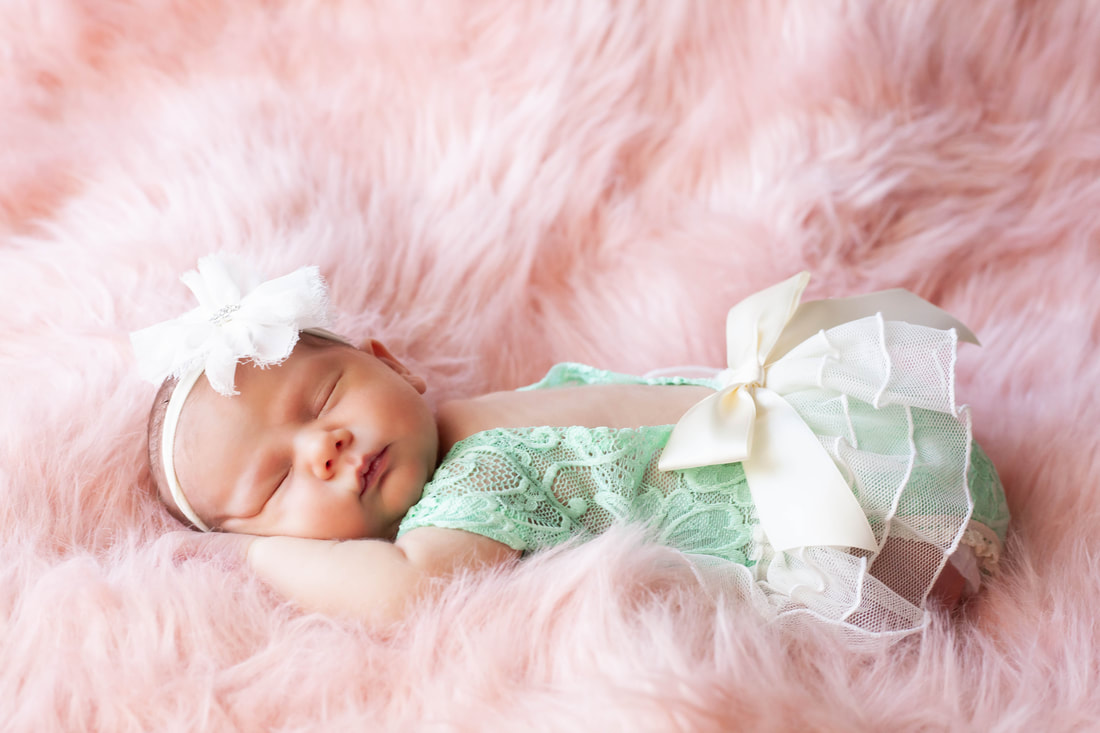 Newborn baby girl in teal lace sleeping on her stomach in a cloud of pink fur