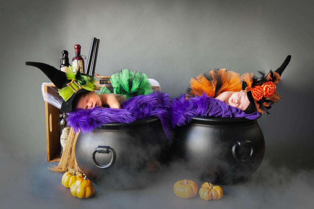 Newborn twin Girls in witch costumes sleep in twin cauldrons Potion bottles and broomsticks are behind them and fog drifts in on the lower part of the photo 