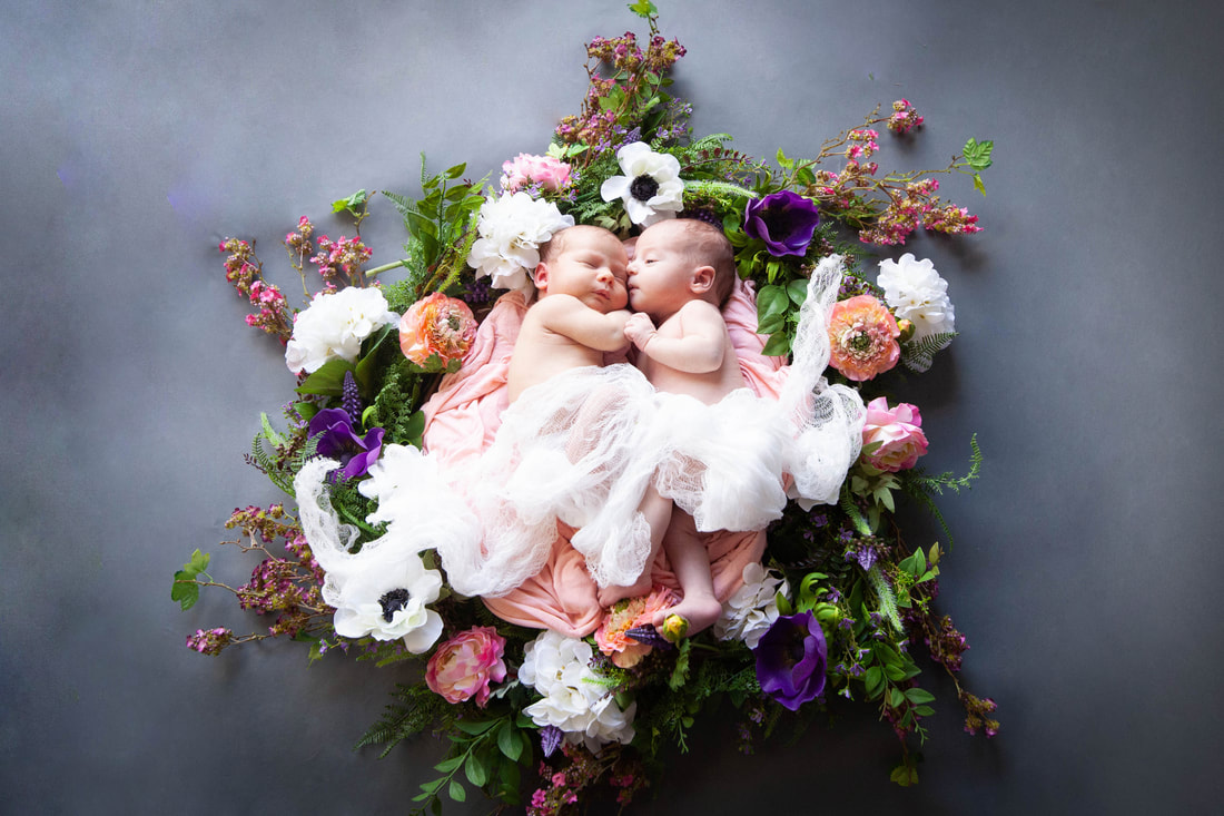 Twin baby girls snuggled close inside a ring of multicolored flowers