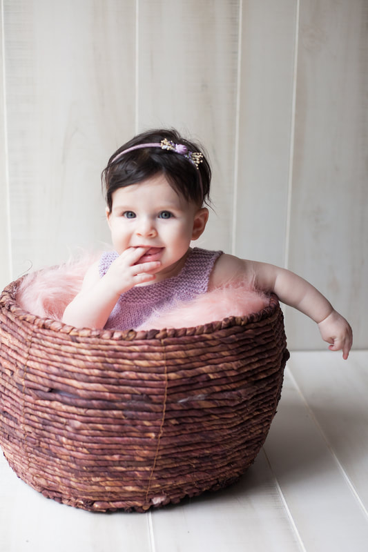 Smiling baby sits in basket at her six month milestone shoot
