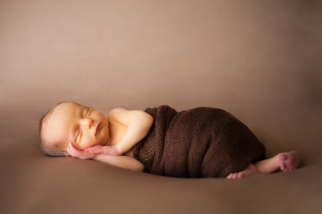 Photograph of newborn baby in brown wrap on a brown background