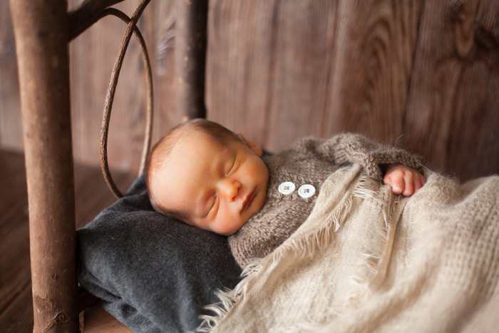 Newborn baby boy photographed lying in rustic bed
