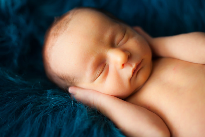 close up photograph of newborn baby boy's face on blue fur