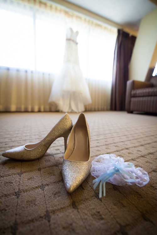 bride's sparkly gold shoes and garter in the foreground with wedding gown in background