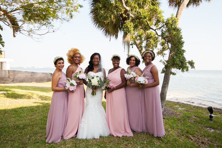 Bride stands on the edge of the water with her bridesmaids