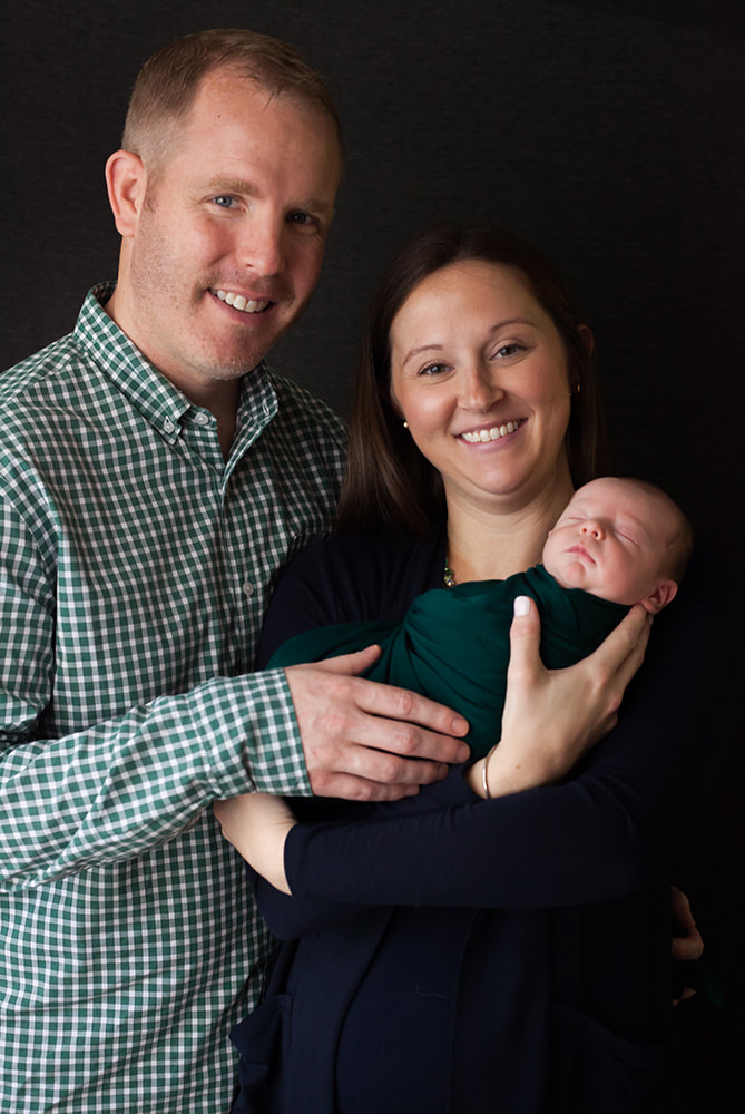 mother and father hold their new baby and smile at the camera