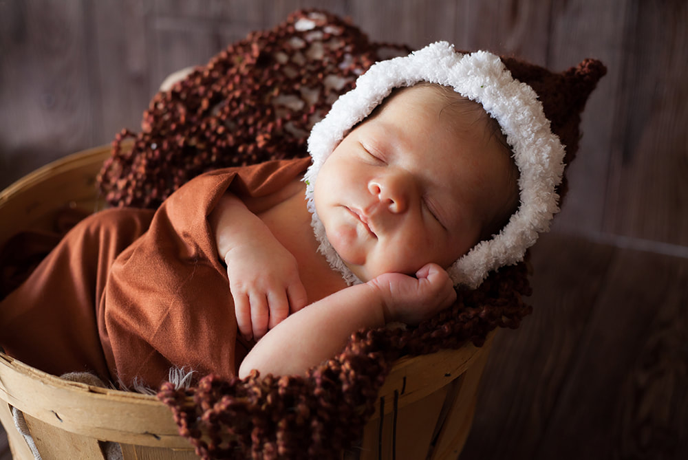 newborn baby sleeping in a basket and wearing fur trimmed bonnet
