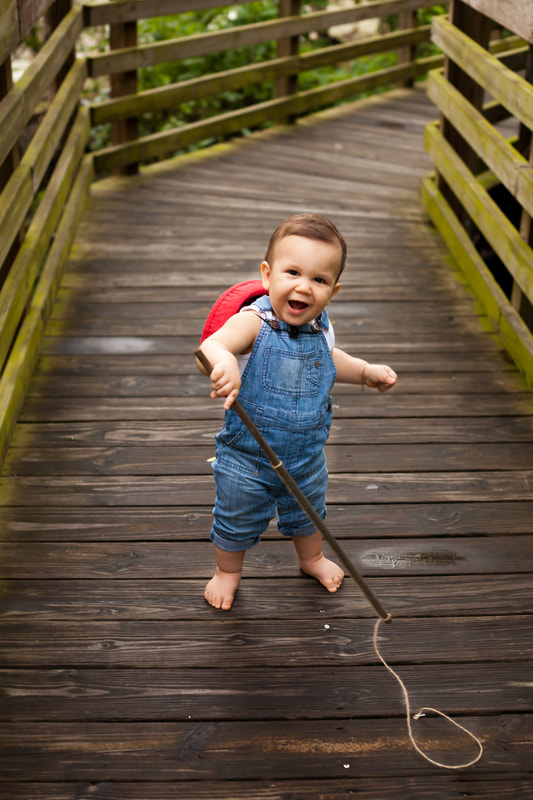 Baby boy in overalls standing on a fishing dock  with stick fishing pole 