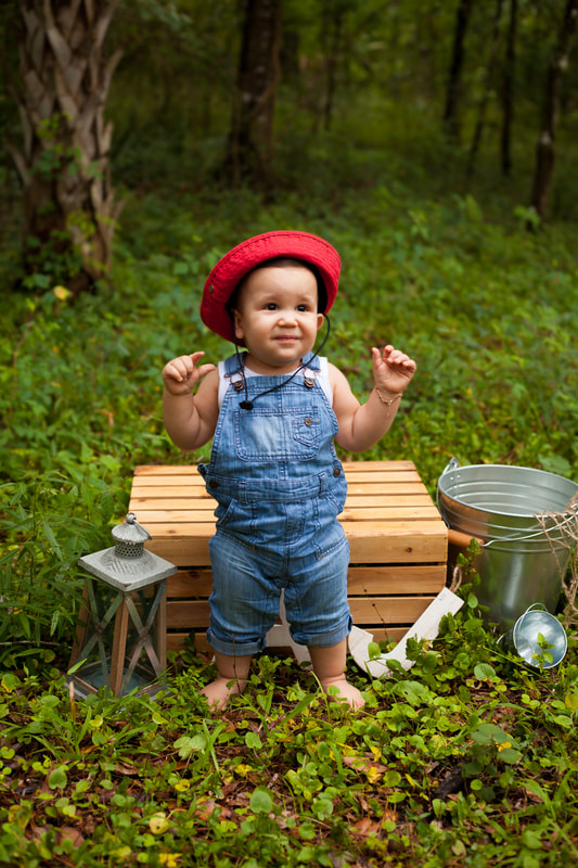 First Birthday boy standing in overalls and red fishing hat