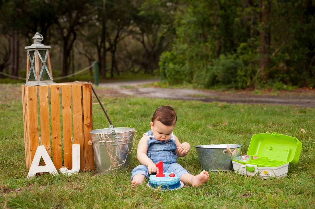 baby boy with his fishing themed first birthday cake in the grass outside