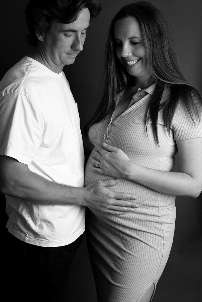 Mother and father to be smile down at mothers pregnant belly 