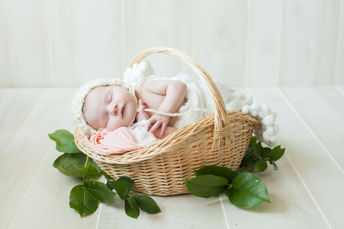 Newborn baby girl in a basket with a white bonnet on