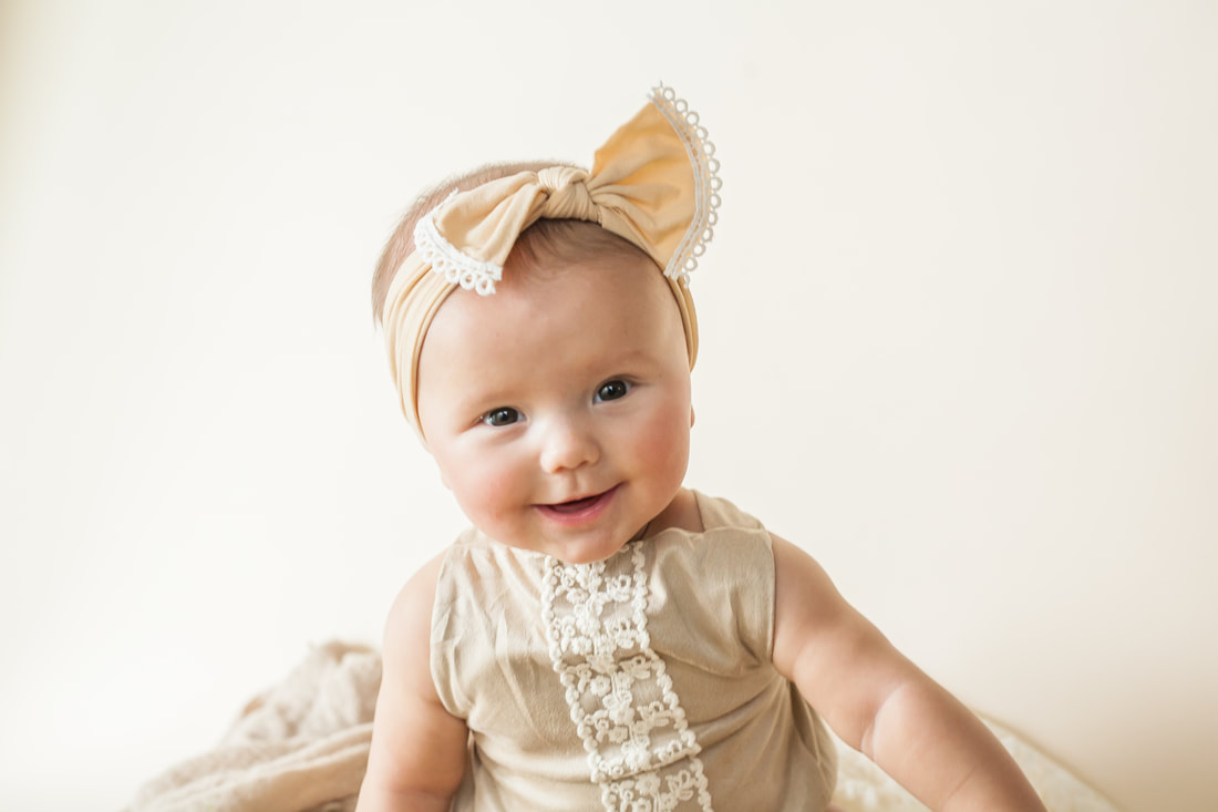 Beautiful baby girl smiling at camera on a bright off white background