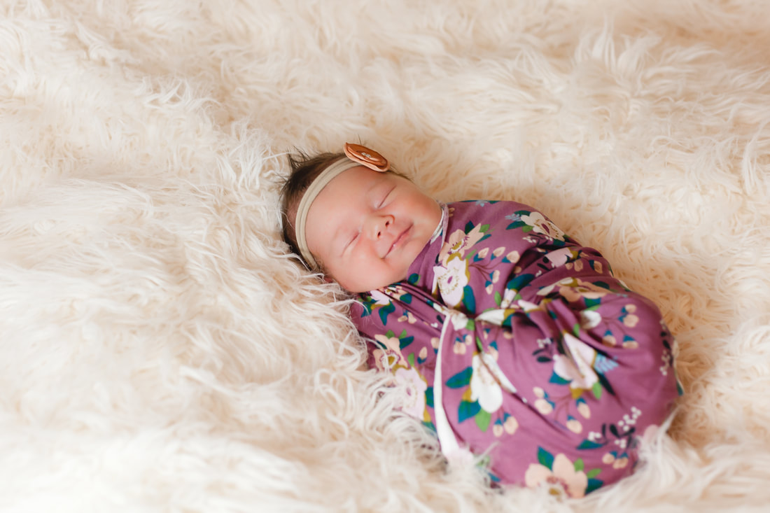 newborn baby girl smiles swaddled in flower patterned wrap