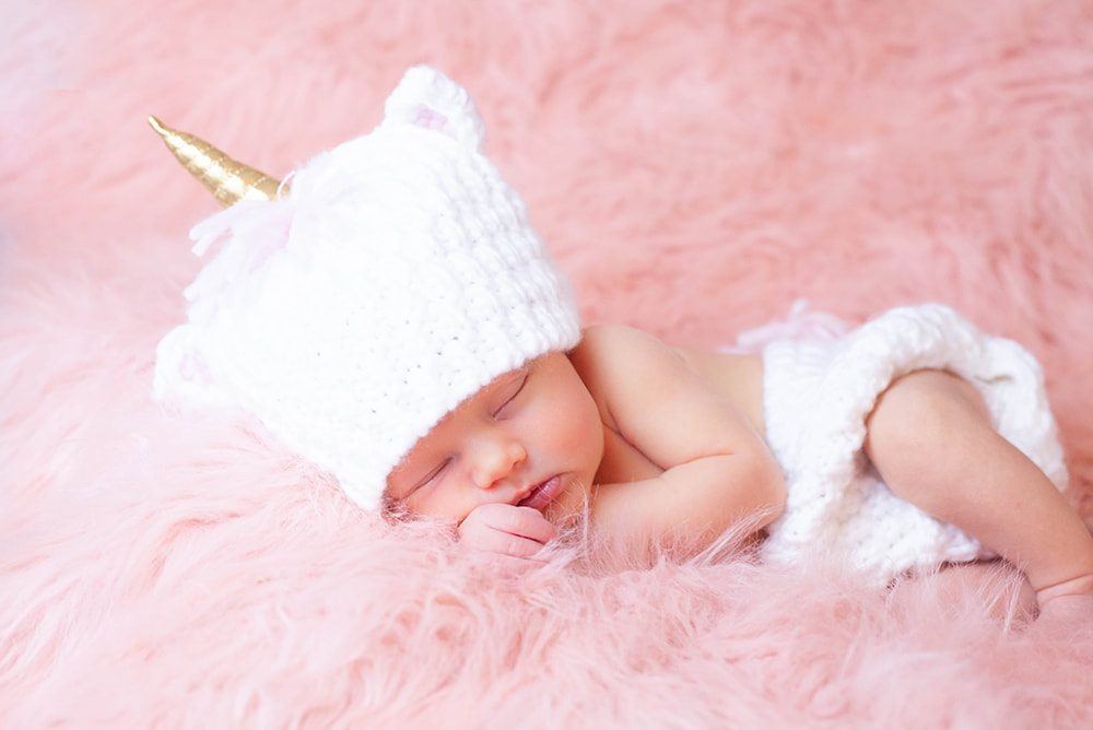 Sleeping Newborn baby girl in a unicorn costume on a cloud of pink 