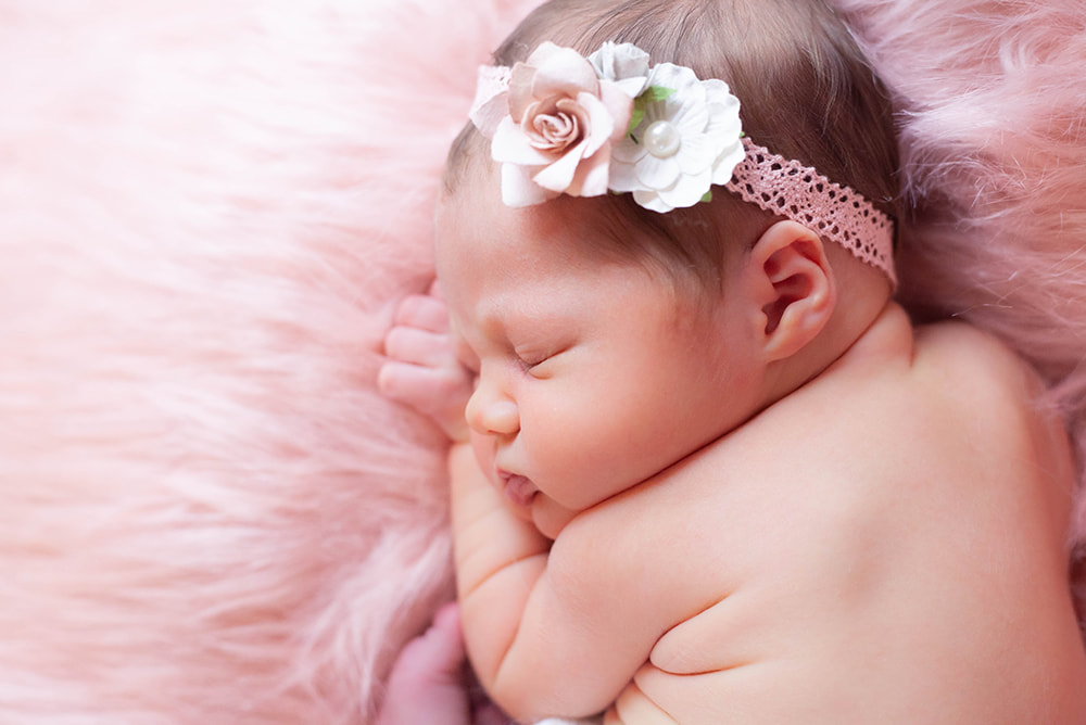 Profile photograph of newborn baby girl sleeping peacefully on pink fur