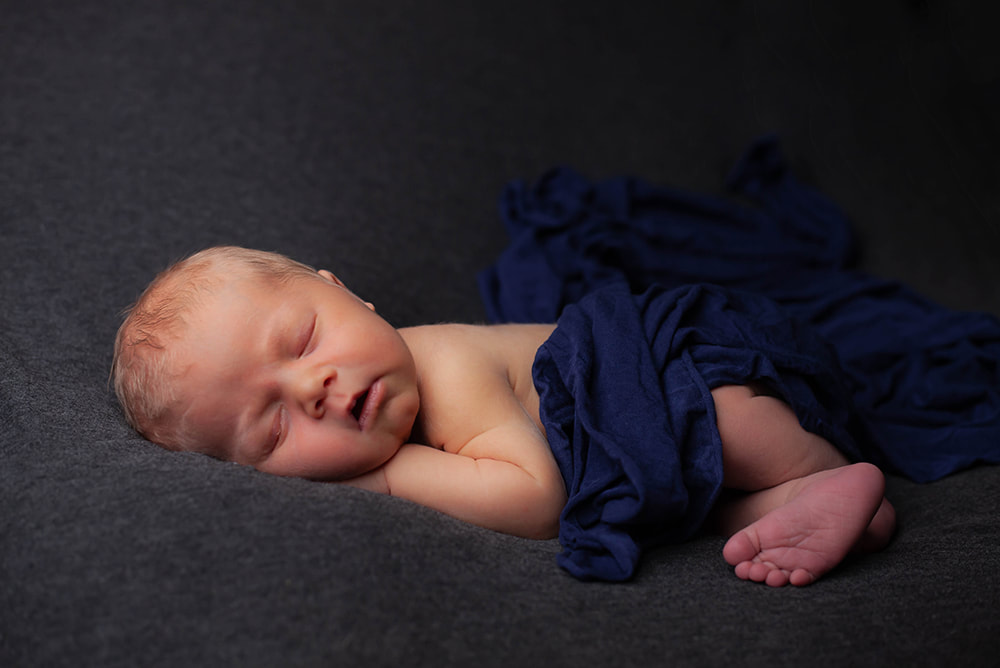 Newborn baby in Tampa sleeping on dark background with navy blue wrap over him