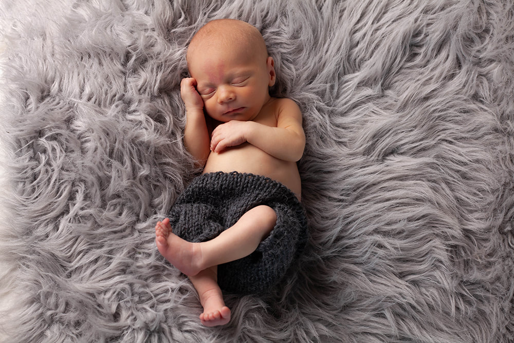 Peacefully sleeping Newborn Baby boy lying on light gray fur seen from above