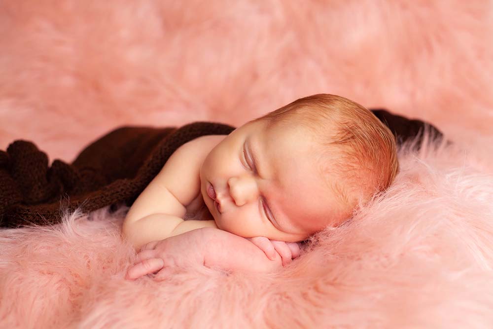 Newborn baby girl on pink fur sleeps with her head resting on her arms