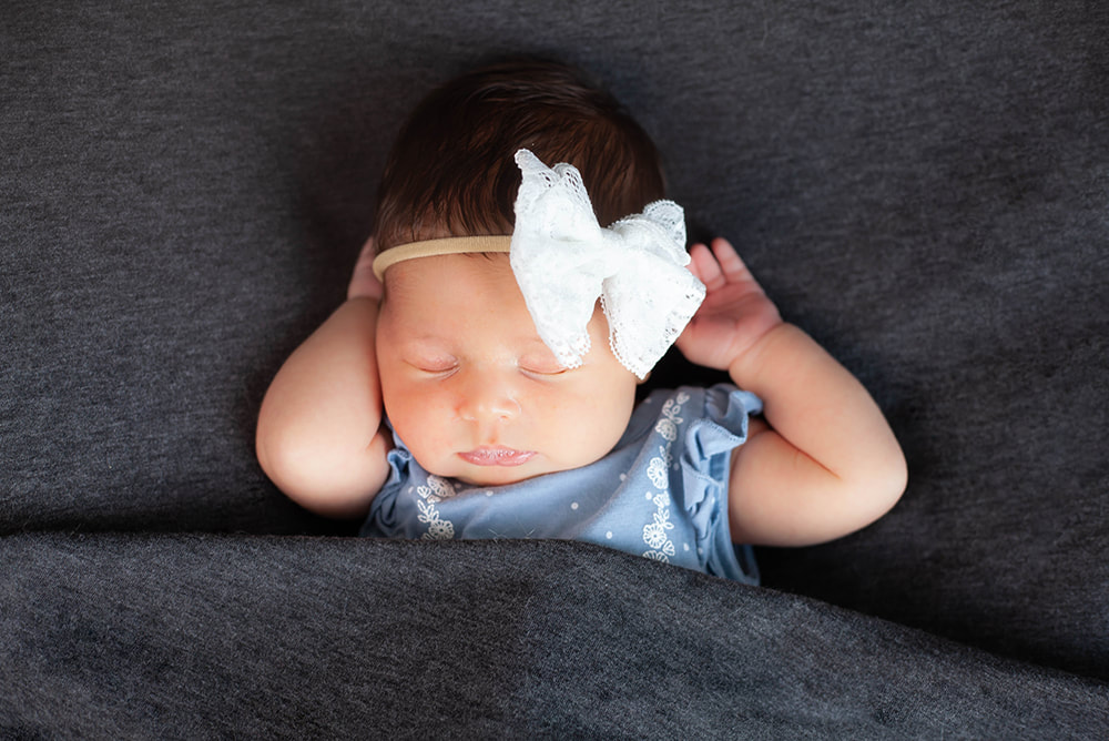 A sleeping newborn baby girl with her hands behind her head on a dark gray blanket