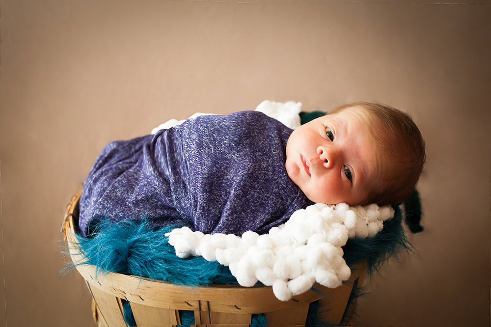 newborn baby swaddled and lying in a basket looks in to the camera 